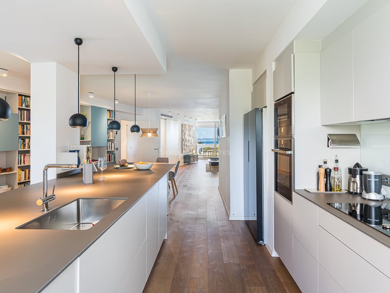 Grand balcon avec vue sur la mer. Balustrade en verre, plancher en bois et mobilier moderne. Éclairage d'ambiance et ciel bleu.