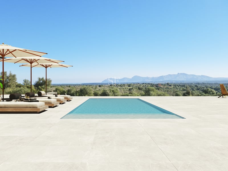Piscine rectangulaire sur une vaste terrasse en pierre dominant un paysage montagneux sous un ciel bleu pur.