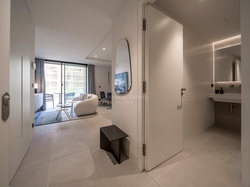 Couloir moderne menant à un salon lumineux avec canapé incurvé et une salle de bain chic sur la droite.