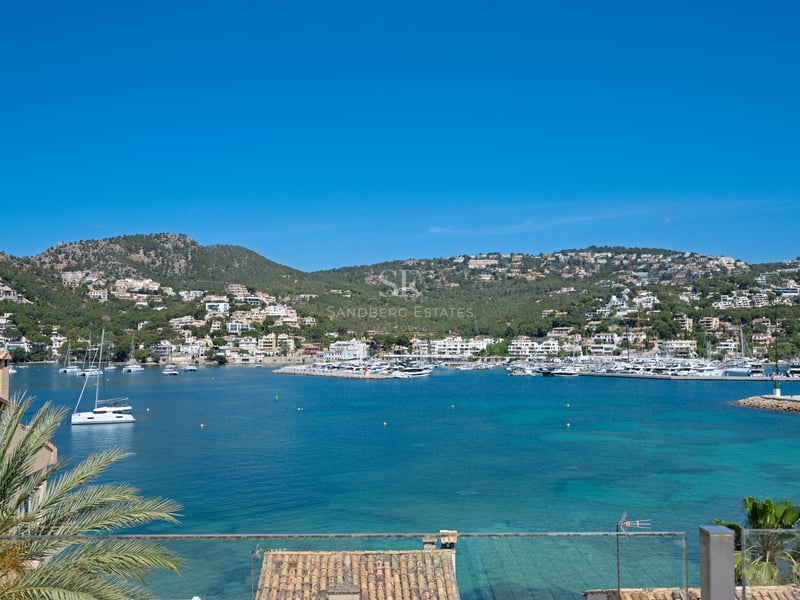 Vue en plongée d'un port méditerranéen turquoise rempli de yachts, entouré de collines vertes et de villas blanches.