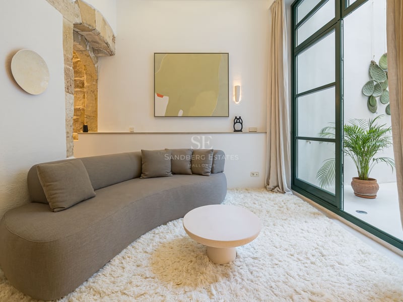 Canapé incurvé taupe sur tapis blanc dans une pièce lumineuse avec arche en pierre et portes vitrées sur patio.