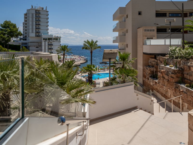 Escaliers extérieurs avec garde-corps en verre surplombant une piscine de complexe et la mer bleue.