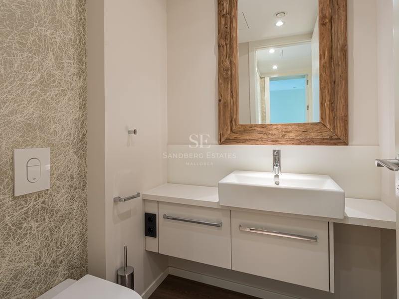 Salle de bain moderne avec vanité blanche, robinetterie chromée et grand miroir à cadre en bois rustique sur papier peint.
