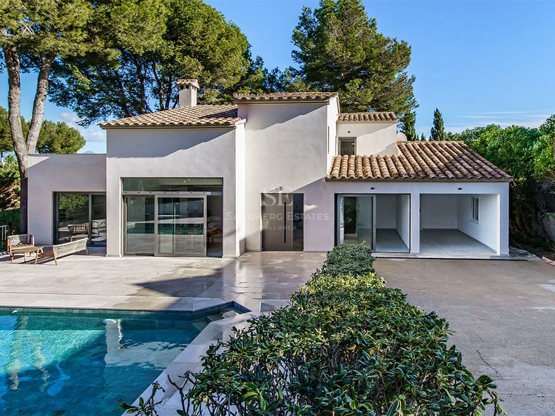 Villa blanche moderne avec piscine turquoise, terrasse en pierre et pins sous un ciel bleu clair.