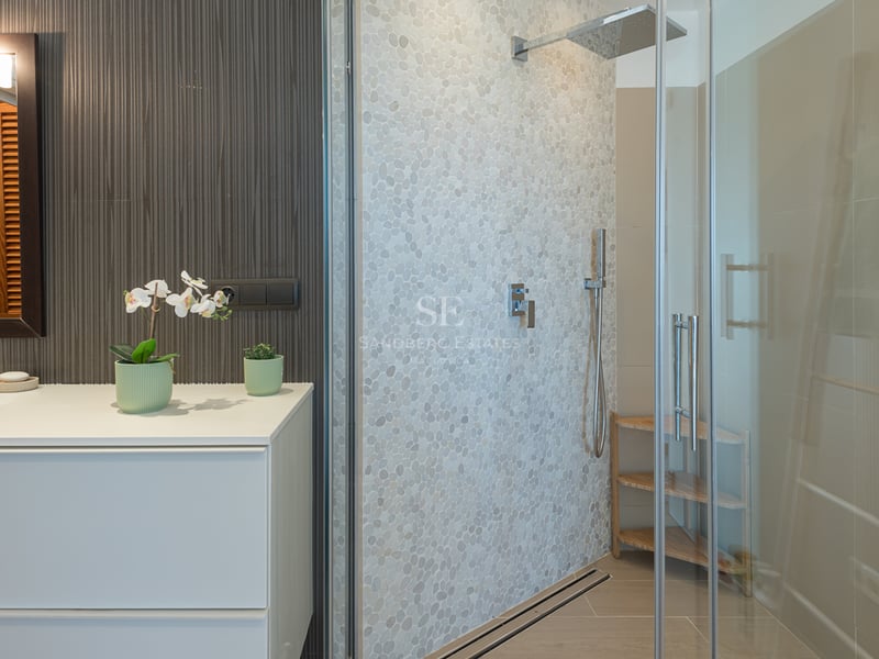Salle de bain contemporaine avec meuble vasque blanc et douche en verre avec mur en galets texturés.