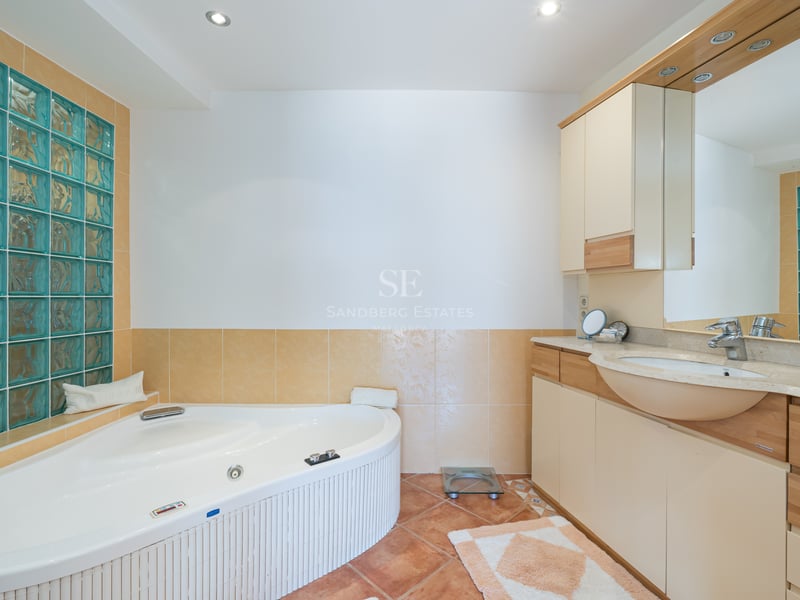 Vue d'une salle de bains avec baignoire balnéo d'angle, briques de verre turquoise et meuble vasque en bois.