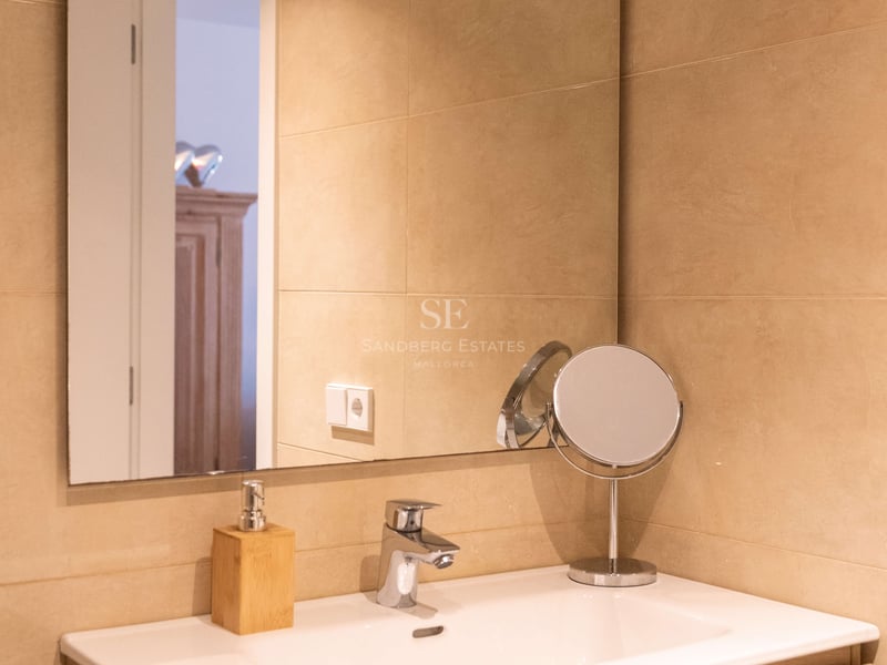 Vasque en céramique blanche sur meuble en bois clair, grand miroir et carrelage mural beige.
