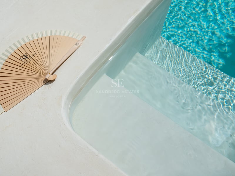 Gros plan de marches de piscine blanches menant à une eau turquoise avec un éventail en bois sur le bord.