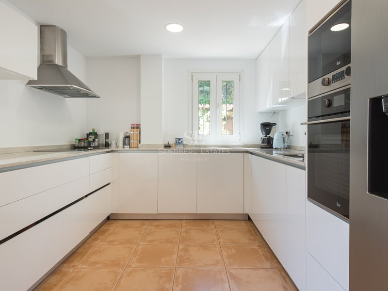 Cuisine moderne en U avec placards blancs brillants, sol en terre cuite et appareils en acier inoxydable.
