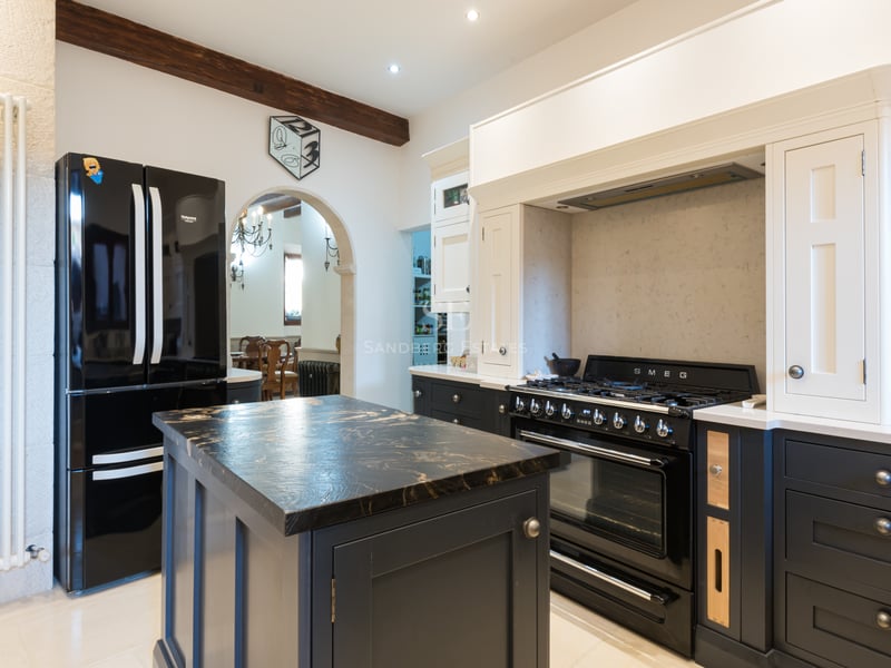 Cuisine moderne rustique avec four SMEG noir, îlot en marbre, poutres en bois et murs en pierre naturelle.
