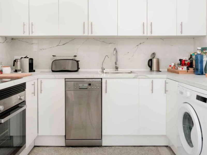 Cuisine blanche moderne avec plan de travail en marbre, lave-vaisselle en inox et rangements épurés.