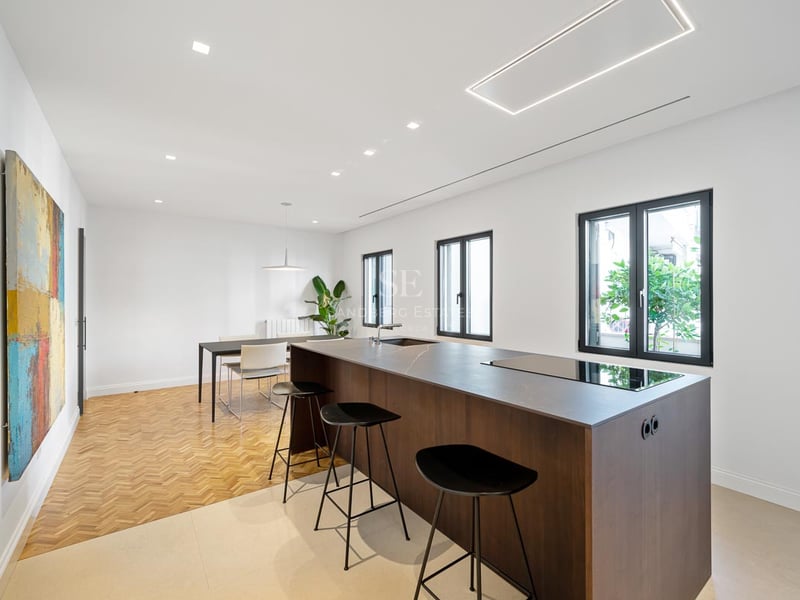 Cuisine minimaliste avec îlot central sombre, tabourets noirs, parquet à chevrons et tableau abstrait coloré.