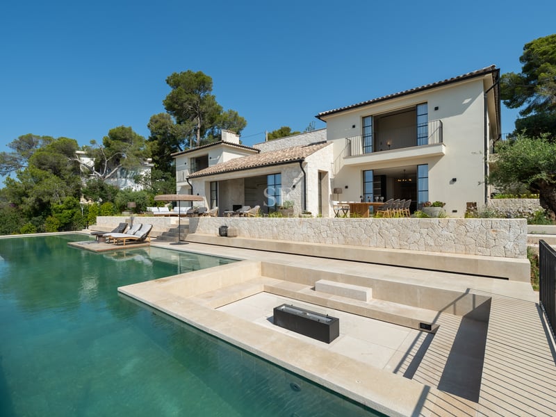 Façade de villa de luxe avec piscine à débordement, salon encastré et murs en pierre naturelle.