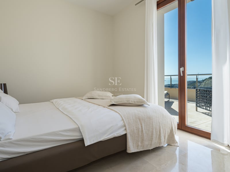 Chambre moderne avec draps blancs, sol en marbre poli et grandes baies vitrées ouvrant sur une terrasse ensoleillée.