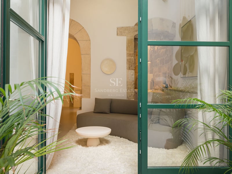 Vue à travers des portes vitrées vertes sur un salon avec canapé incurvé, tapis blanc et arches en pierre.