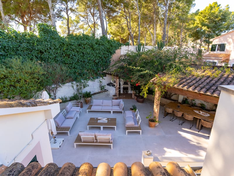 Vue surélevée d'une spacieuse terrasse pavée avec des canapés blancs, une grande table à manger en bois et des murs végétalisés.