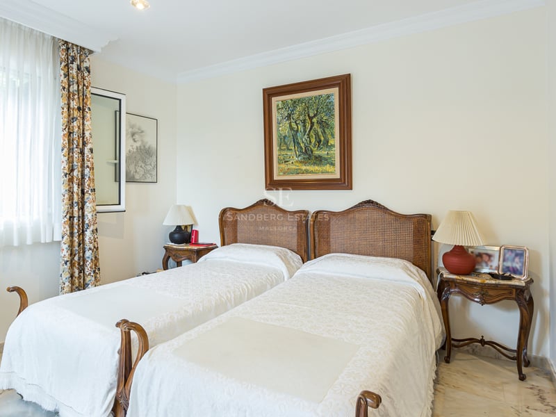 Chambre avec deux lits simples, têtes de lit en rotin, sol en marbre et tableaux au mur.