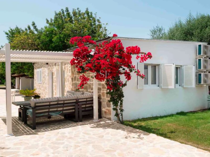 Bâtiment blanc avec façade en pierre, bougainvillier rouge et pergola moderne sur une terrasse aménagée.