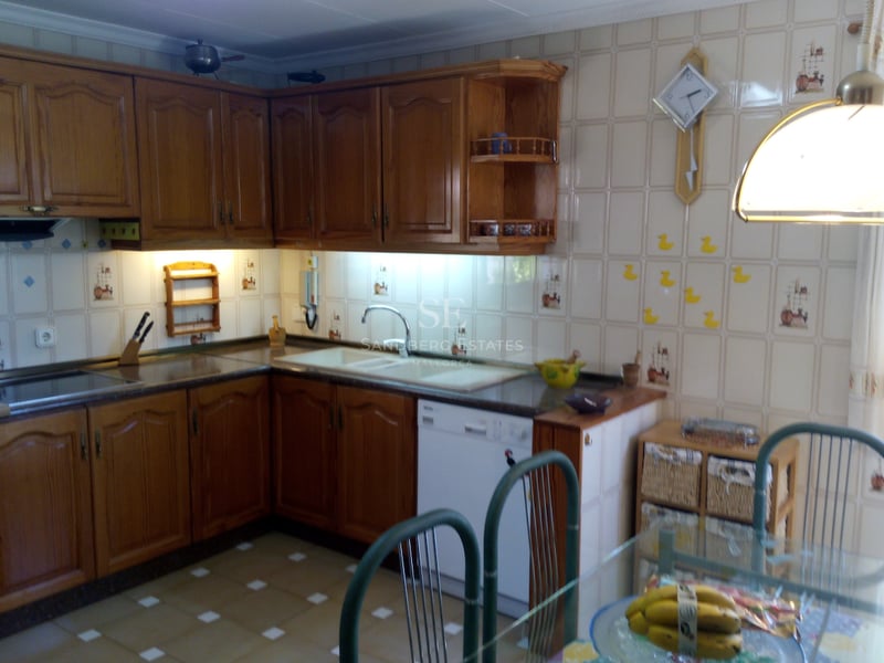 Cuisine en L avec des meubles en chêne miel, du carrelage mural décoratif et un coin repas.