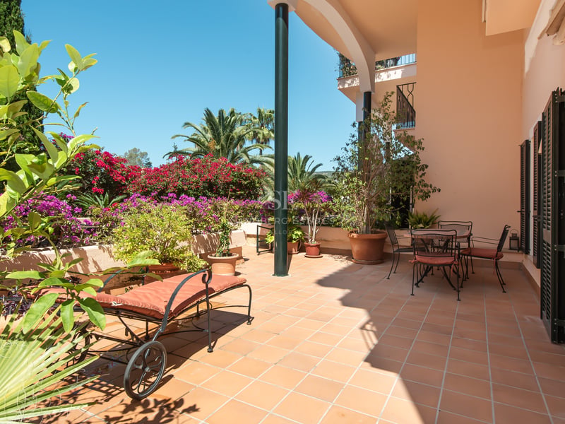 Terrasse en terre cuite avec chaise longue et coin repas, entourée de bougainvilliers et de palmiers sous un ciel bleu.