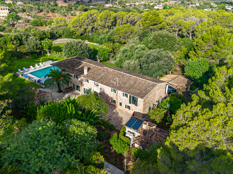 Vue aérienne d'une grande maison de campagne en pierre et d'une piscine entourée d'une forêt de pins.