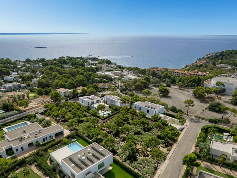 Vue de drone en hauteur de villas blanches contemporaines nichées dans la verdure avec vue panoramique sur la mer.