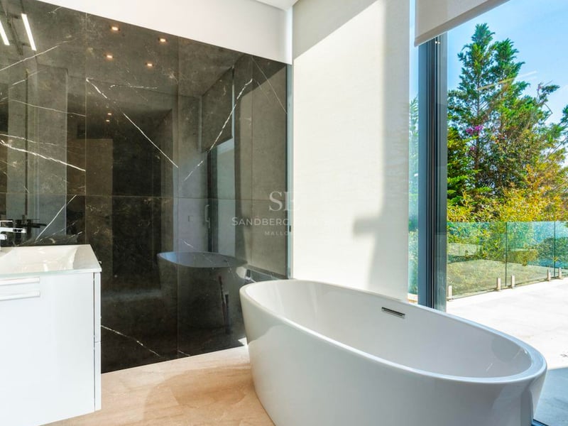 Salle de bain moderne dotée d'une baignoire îlot blanche devant une grande baie vitrée avec vue sur la verdure.
