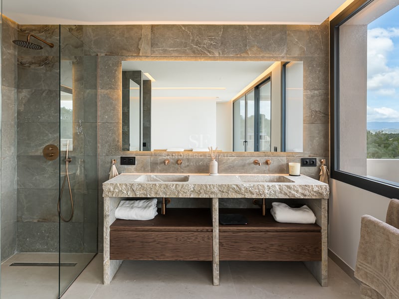 Salle de bains de luxe avec double vasque en pierre naturelle, grand miroir rétroéclairé et finitions en bois sombre.