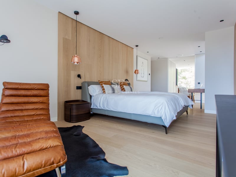 Chambre principale contemporaine avec boiseries, chaise longue en cuir fauve et suspensions en cuivre.