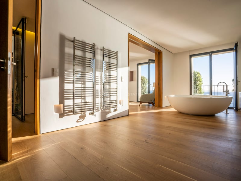 Salle de bains de maître minimaliste avec parquet en chêne, baignoire îlot ovale, sèche-serviettes chromés et vue sur mer.