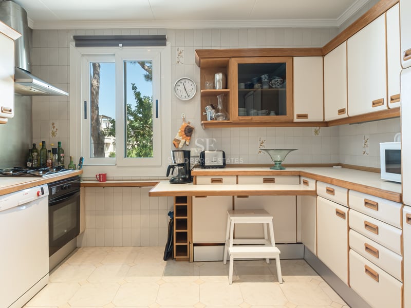 Cuisine claire avec placards blancs, finitions en bois, plan de travail fonctionnel et fenêtre sur le jardin.