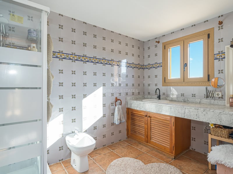 Salle de bain avec carreaux décoratifs, plan en marbre blanc, meuble en bois, bidet et sol en terre cuite.