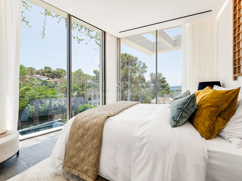 Chambre principale contemporaine avec de grandes baies vitrées donnant sur des palmiers et de la verdure.