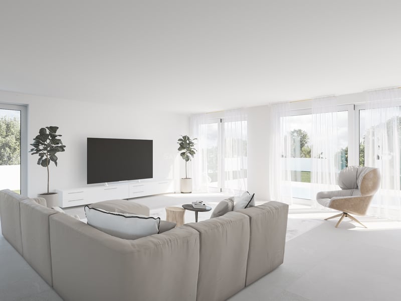 Salon lumineux avec canapé beige, baies vitrées et vue sur un jardin avec piscine.