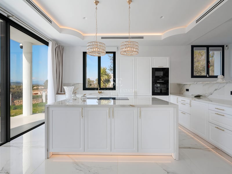 Cuisine moderne lumineuse avec grand îlot en marbre, finitions dorées et baies vitrées donnant sur le jardin.