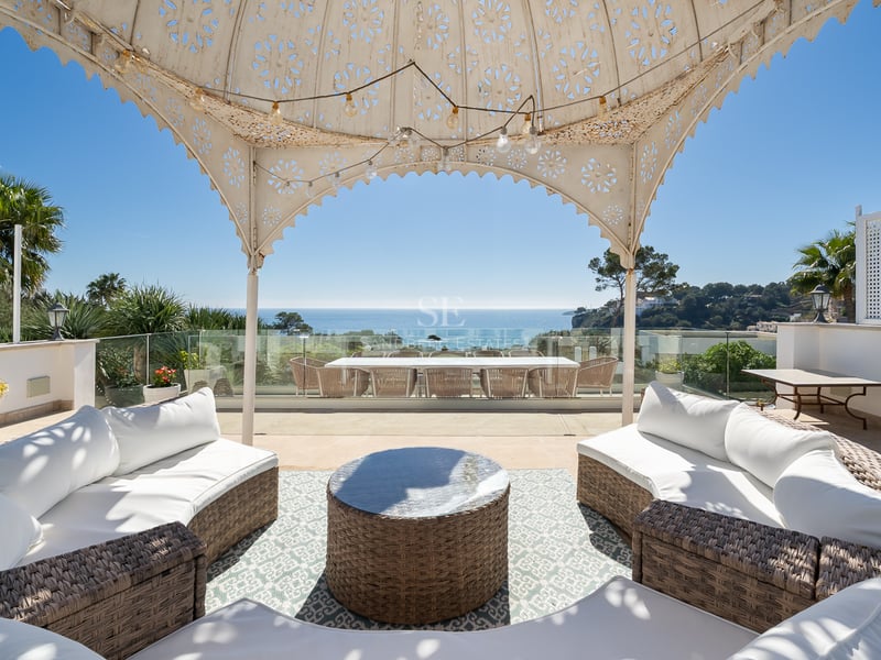 Grande terrasse avec canapés en osier sous un pavillon décoratif offrant une vue imprenable sur l'océan.