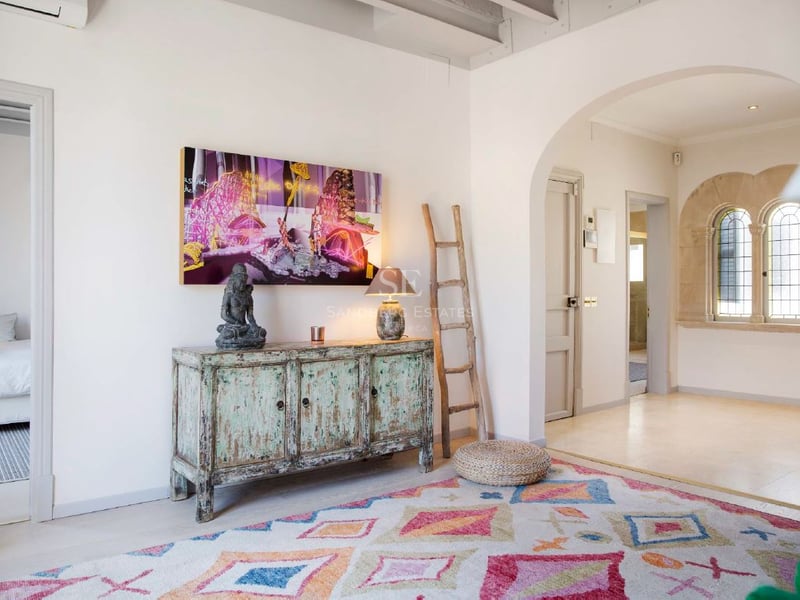 Pasillo interior con alfombra geométrica, aparador turquesa vintage, escalera rústica y ventanas de piedra en arco.