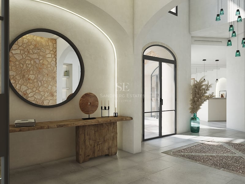 Entrada de villa con arcos, pared de piedra natural, espejo circular y consola de madera tallada.
