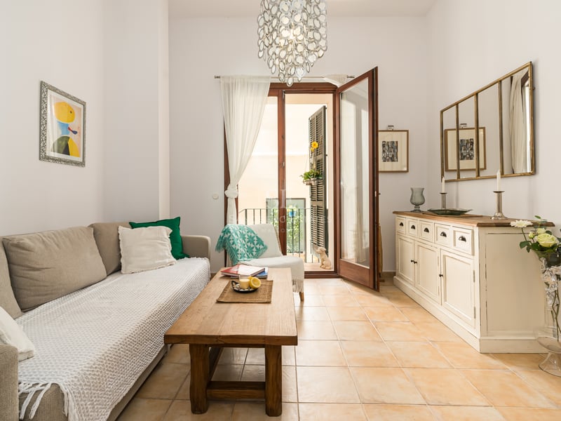 Salon baigné de lumière avec sol en terre cuite, canapé beige, table en bois et portes-fenêtres ouvrant sur un balcon.