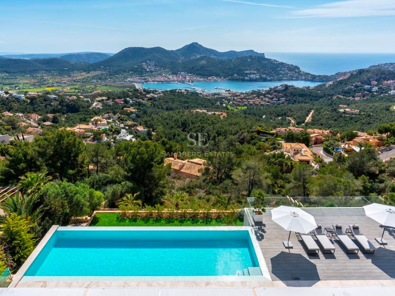 Une piscine à débordement et une terrasse ensoleillée surplombant une vallée et une baie méditerranéenne.