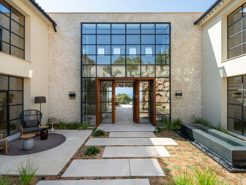 Entrée principale d'une villa de luxe avec murs en pierre, grandes baies vitrées et porte pivotante en bois massif.