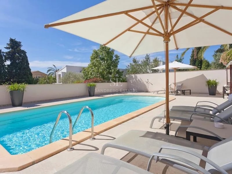Piscine turquoise entourée d'une terrasse en pierre avec bains de soleil et parasols blancs.