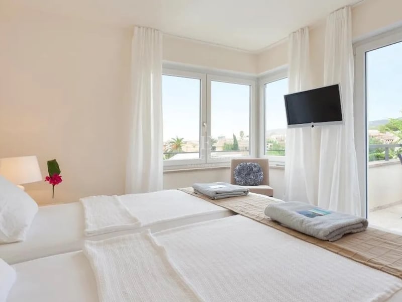 Chambre moderne avec deux lits, draps blancs, grandes fenêtres et porte vitrée ouvrant sur une terrasse ensoleillée.