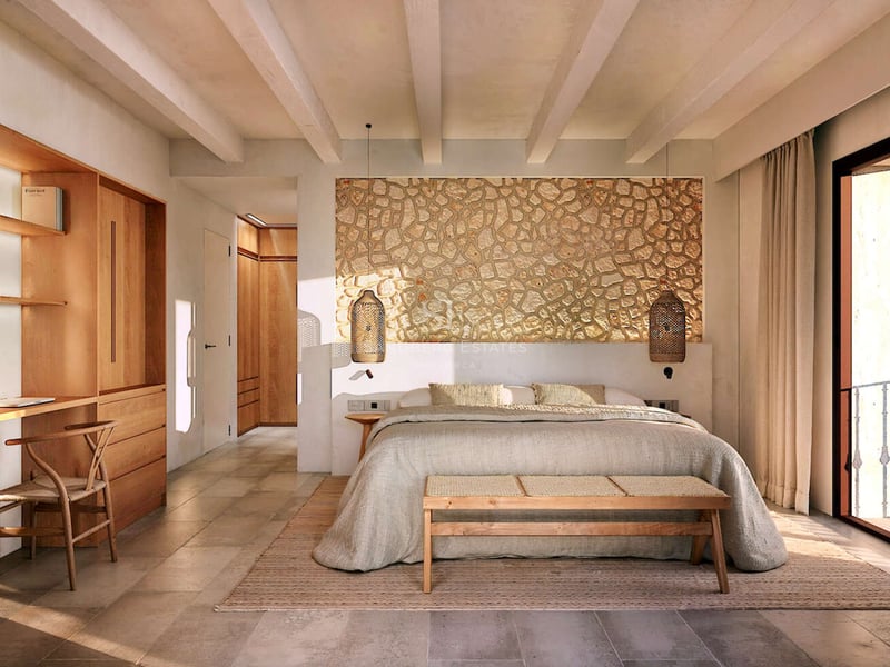 Chambre de luxe avec mur en pierre, poutres apparentes, bureau intégré en bois et porte-fenêtre.