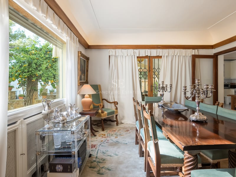 Salle à manger formelle avec table en bois poli, chaises vertes et candélabres en argent devant une grande fenêtre.