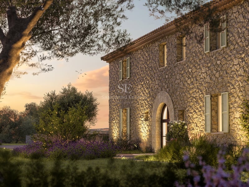 Façade en pierre d'une villa de luxe au coucher du soleil avec entrée voûtée et oliviers.