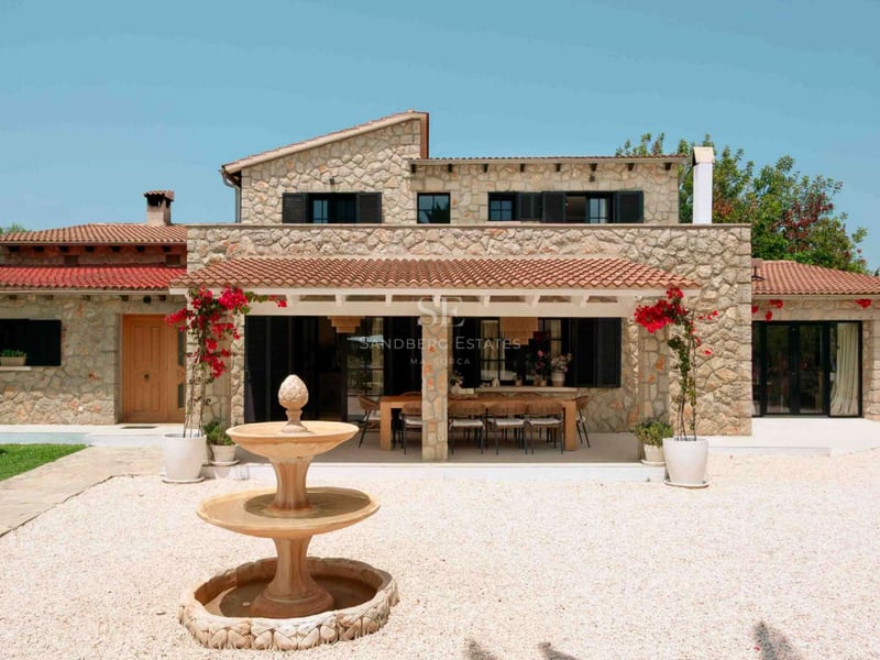 Extérieur d'une villa en pierre avec toit en terre cuite, porche couvert avec salle à manger et fontaine.