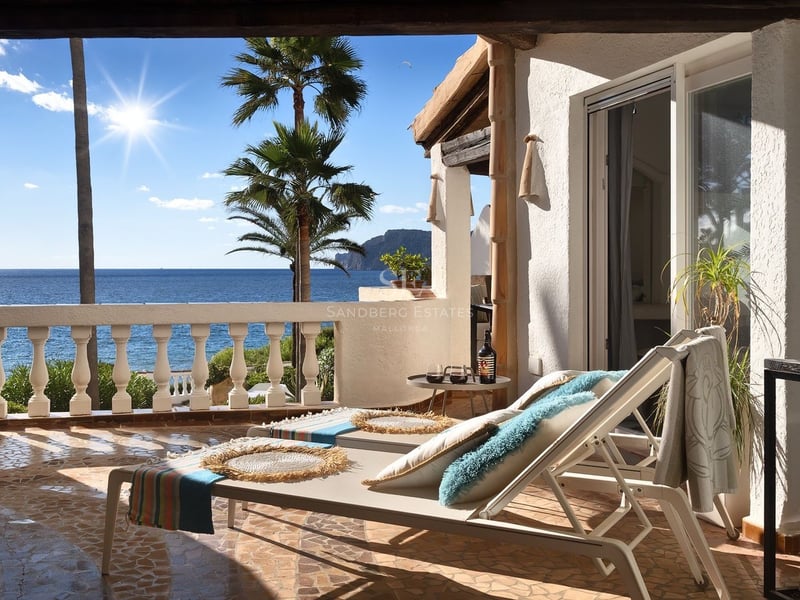 Chaises longues blanches sur une terrasse méditerranéenne surplombant l'océan avec palmiers sous un soleil éclatant.