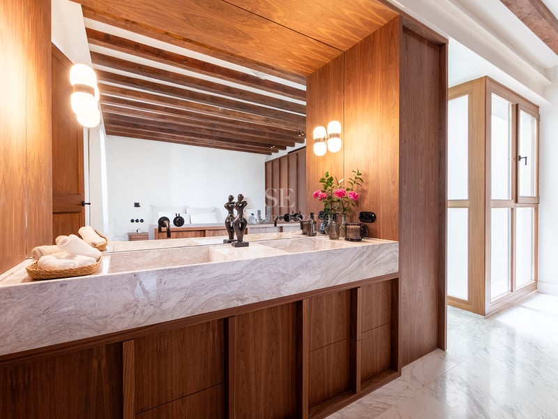 Baño principal moderno con lavabo doble de mármol, muebles de nogal y vigas de madera vistas.