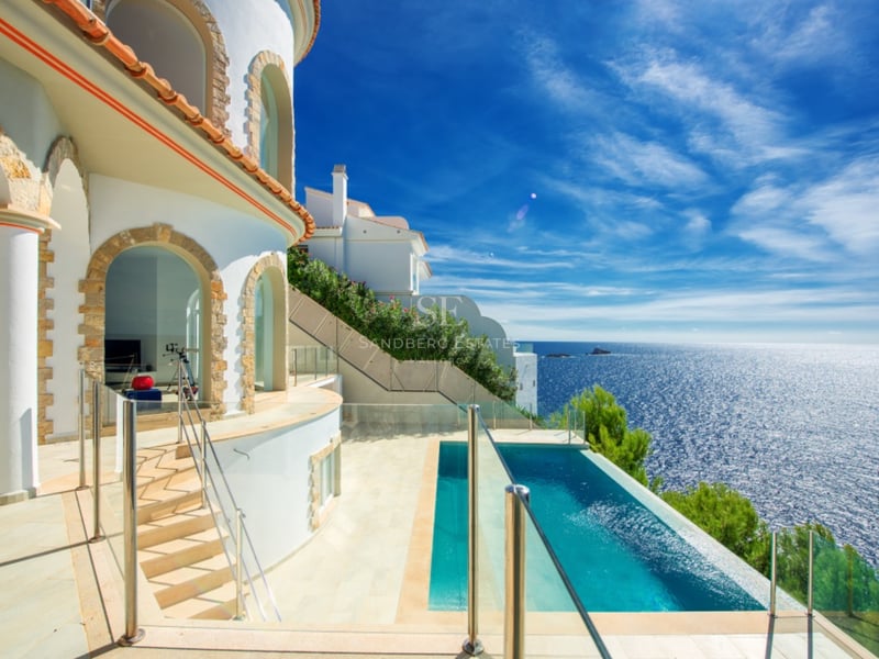 Villa méditerranéenne blanche avec piscine à débordement donnant sur la mer sous un ciel bleu.